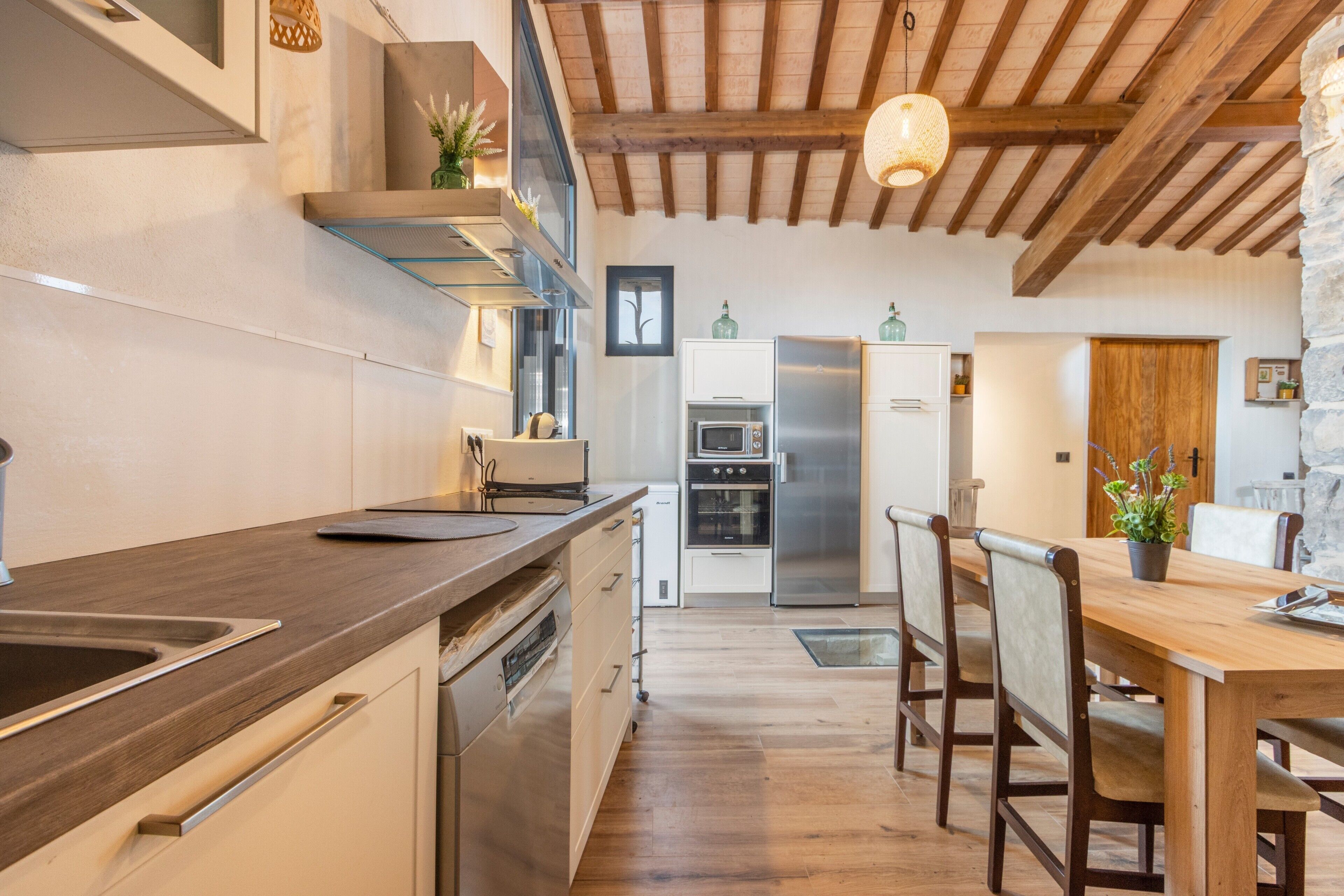 A modern kitchen with wooden beams, stainless steel appliances, and a dining area with wooden chairs and a table.