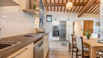 A modern kitchen with wooden beams, stainless steel appliances, and a dining area with wooden chairs and a table.