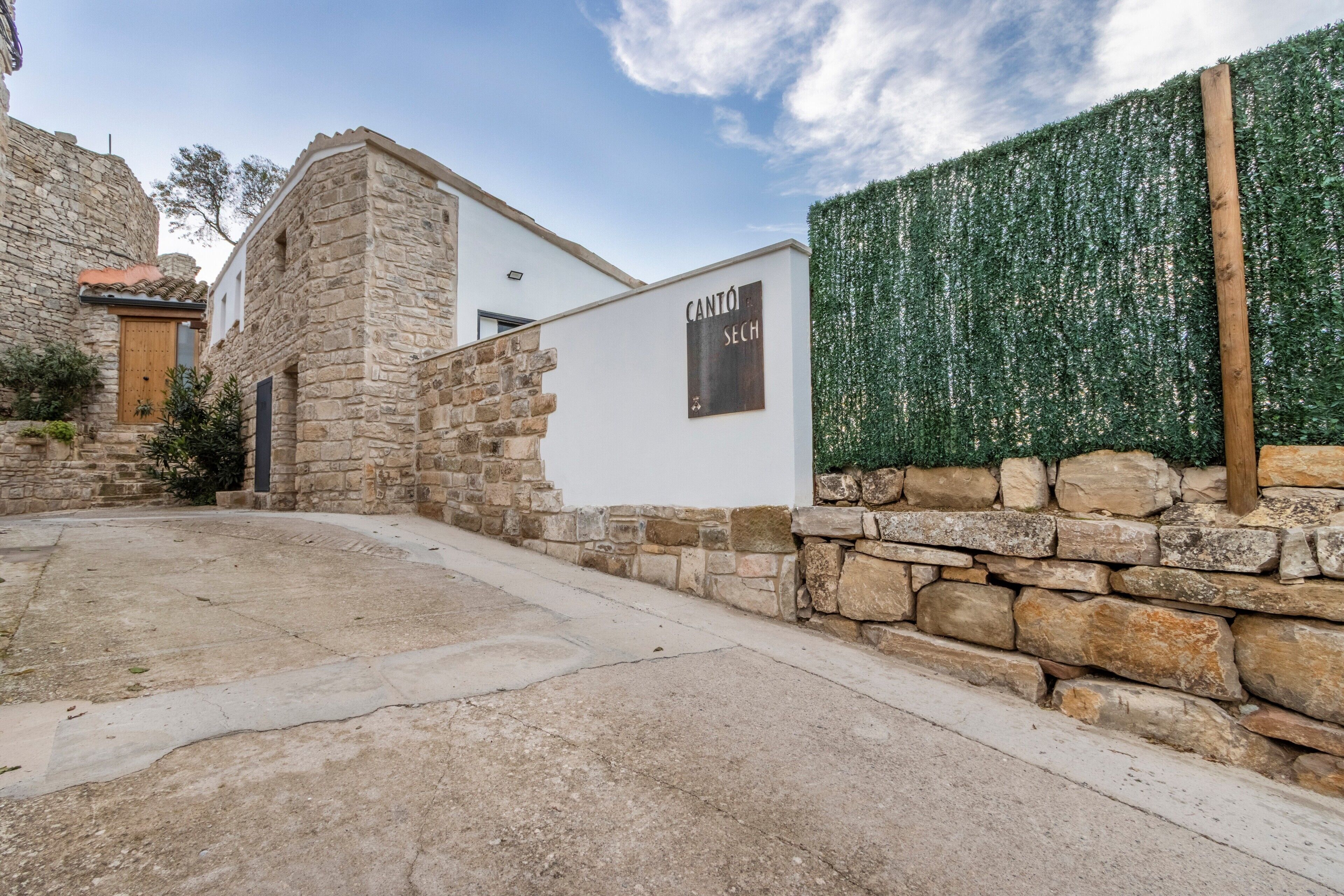A stone building with a white facade, a wooden door, and a sign that reads 'CANTÓ SECH'.