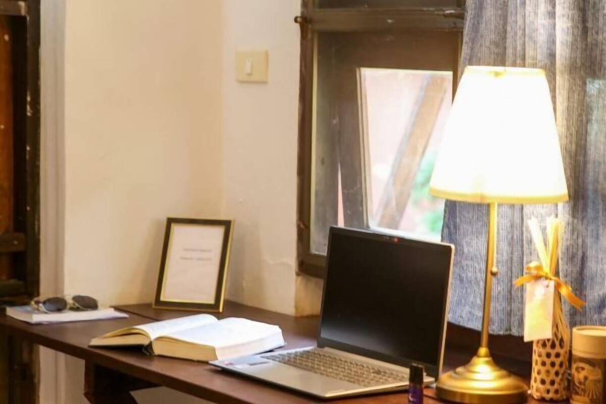 Un bureau avec un ordinateur portable, un livre ouvert, un certificat encadré et une lampe.