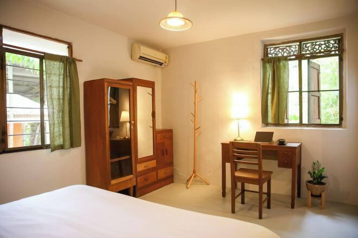 Une chambre à coucher comprenant un lit, un bureau avec une chaise, une armoire et une fenêtre avec des rideaux.
