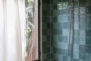 Een badkamer met een glazen douchecabine, een raam met gordijn en een betegelde muur.