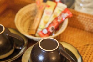 Een close-up van een theepot en kopjes op een tafel met een mand vol lekkernijen.