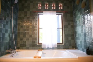 Un baño con bañera, una ventana con cortina y zona de ducha.