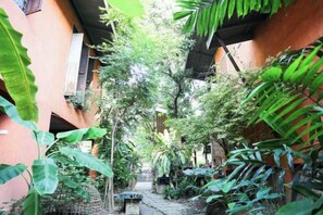 A narrow courtyard with a stone bench, surrounded by lush greenery and buildings with orange walls. - Baannoi Retreat and Stay Chiang Mai (Chiang Mai)