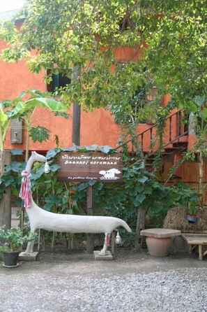 Un espacio exterior rústico con un letrero de madera, una estatua de cabra blanca y plantas en macetas.