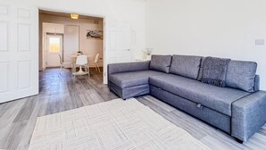 En moderne stue med en grå hjørnesofa, en hvid måtte og et spiseområde med bord og stole.