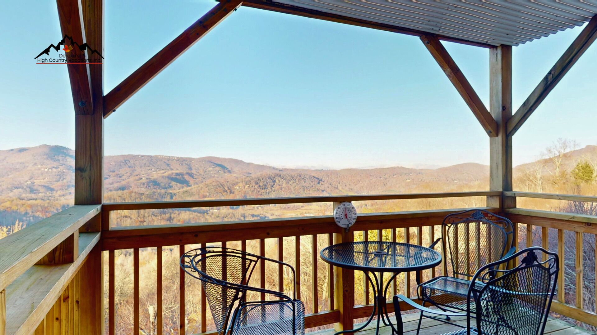 A wooden deck with metal chairs and a table, overlooking a mountainous landscape.