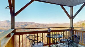 Un terrazzo in legno con sedie e tavolo in metallo, con vista su un paesaggio montuoso.