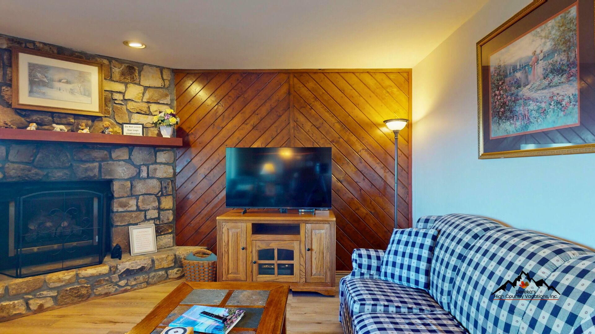 Una sala de estar acogedora con chimenea de piedra, un televisor sobre un soporte de madera y un sofá a cuadros.