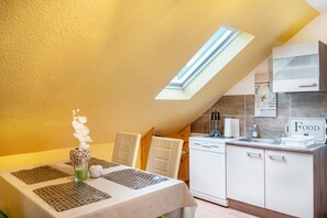 Un coin repas avec une table dressée pour deux personnes, une cuisine avec des meubles blancs et une lucarne.