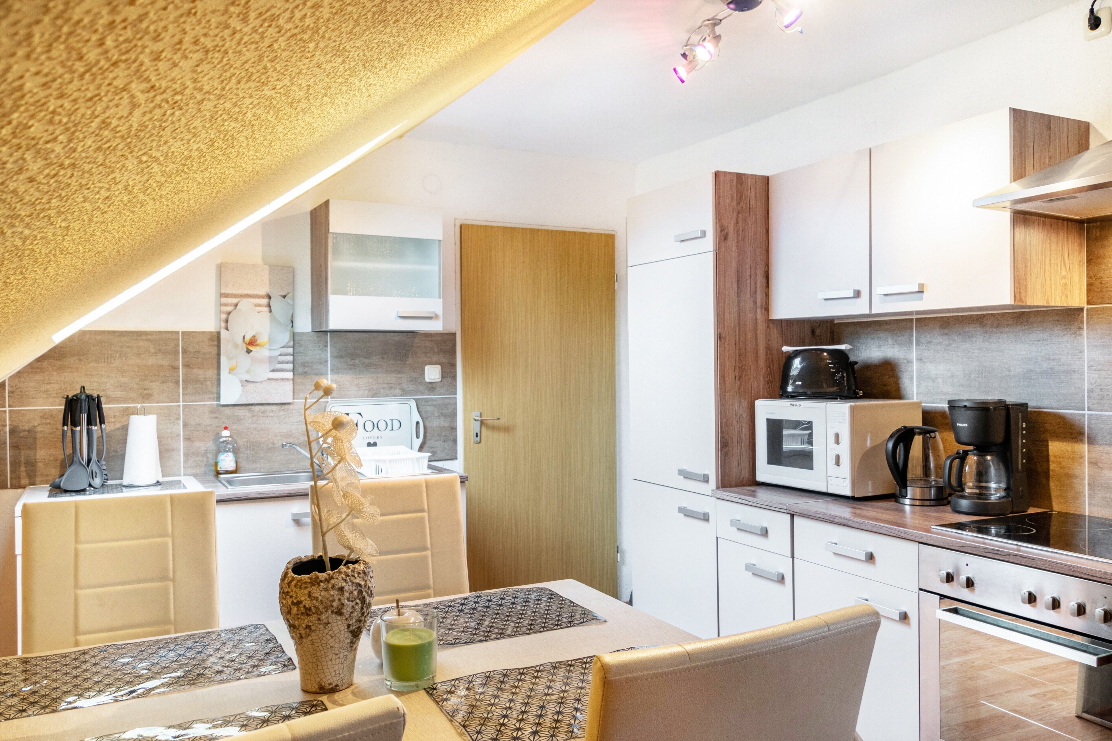 A modern kitchen with white cabinets, a microwave, a coffee maker, and a dining area with a table and chairs.