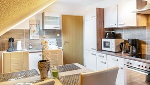 Een moderne keuken met witte kasten, een magnetron, een koffiezetapparaat en een eethoek met een tafel en stoelen.
