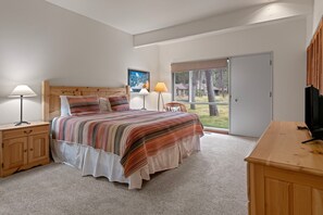 Ein Schlafzimmer mit einem großen Bett, einem Holzkopfende, einem Nachttisch mit Lampe, einem Fernsehschrank und einer Schiebetür zu einem Balkon.