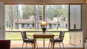 A room with a large sliding glass door leading to a deck. There is a wooden table with two chairs and a table lamp. - The Meadow House in Sunriver (Sunriver)