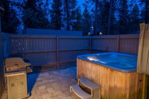Ein Whirlpool in einem Garten mit Holzzaun, Grill und Warmwasserbereiter.