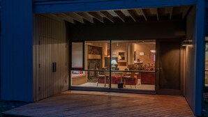 A modern building with a wooden exterior and a glass door leading to an interior space with a dining area and kitchen. - The Meadow House in Sunriver (Sunriver)