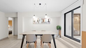 A modern dining area with a wooden table and chairs, a large window, and a wall-mounted light fixture. - GuestReady - Charming Porto's nook (Porto)