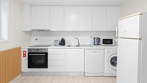 A modern kitchen with white cabinets, a dishwasher, a washing machine, a microwave, and a kettle. - GuestReady - Charming Porto's nook (Porto)