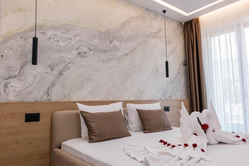 Une chambre d’hôtel avec un mur en marbre, un lit avec des oreillers blancs et bruns, et une table de chevet agrémentée d’un arrangement floral.