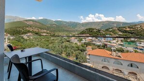 A balcony with a table and chairs, overlooking a town with mountains in the background. - Sun George (Himare)