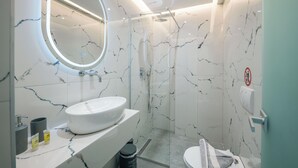 A modern bathroom with a white marble sink, a round mirror, and a glass-enclosed shower. - Sun George (Himare)