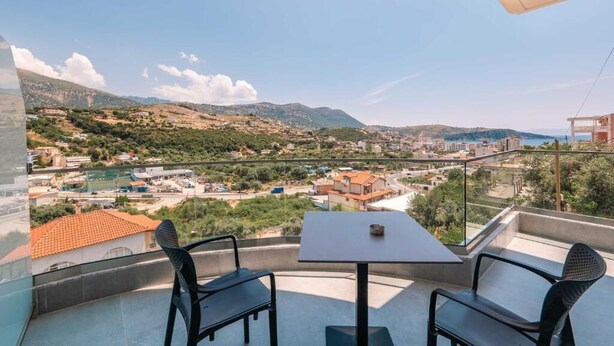 A balcony with a table and chairs, overlooking a town with buildings and hills. - Sun George (Himare)