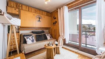 A cozy room with a bed, a small wooden table, a window with curtains, and a view of a snowy landscape.