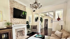 Una sala de estar con chimenea, televisor montado en una pared de ladrillo, candelabro y una escalera que sube a otro nivel.
