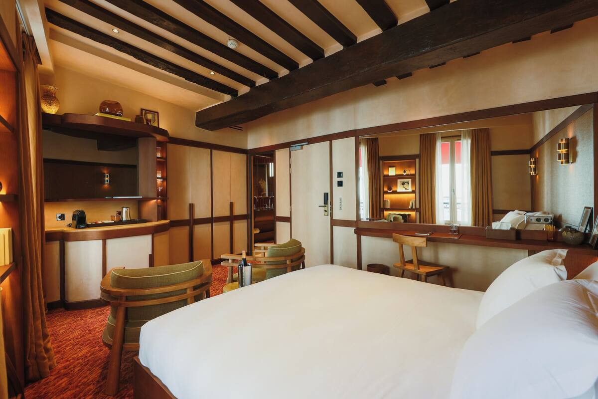 A hotel room with a large bed, a desk with a chair, a small table, and a mirror.