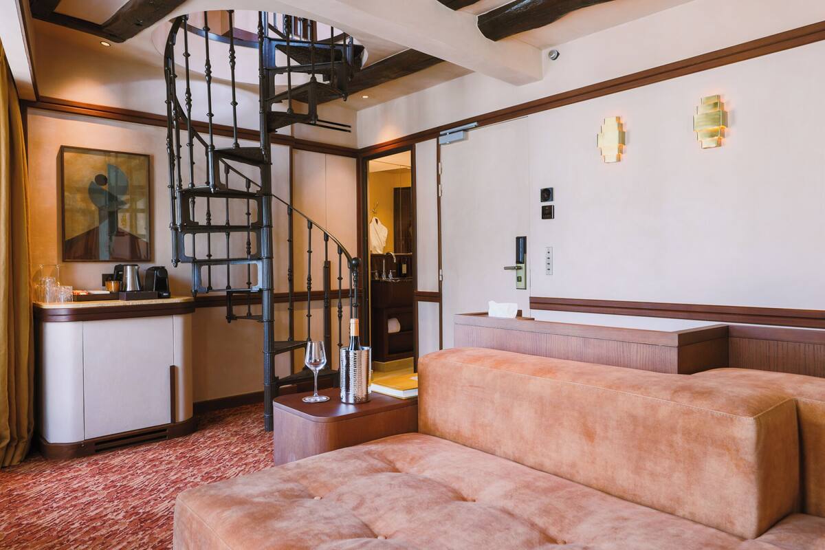 A hotel room with a staircase, a sofa, a minibar, and a painting on the wall.