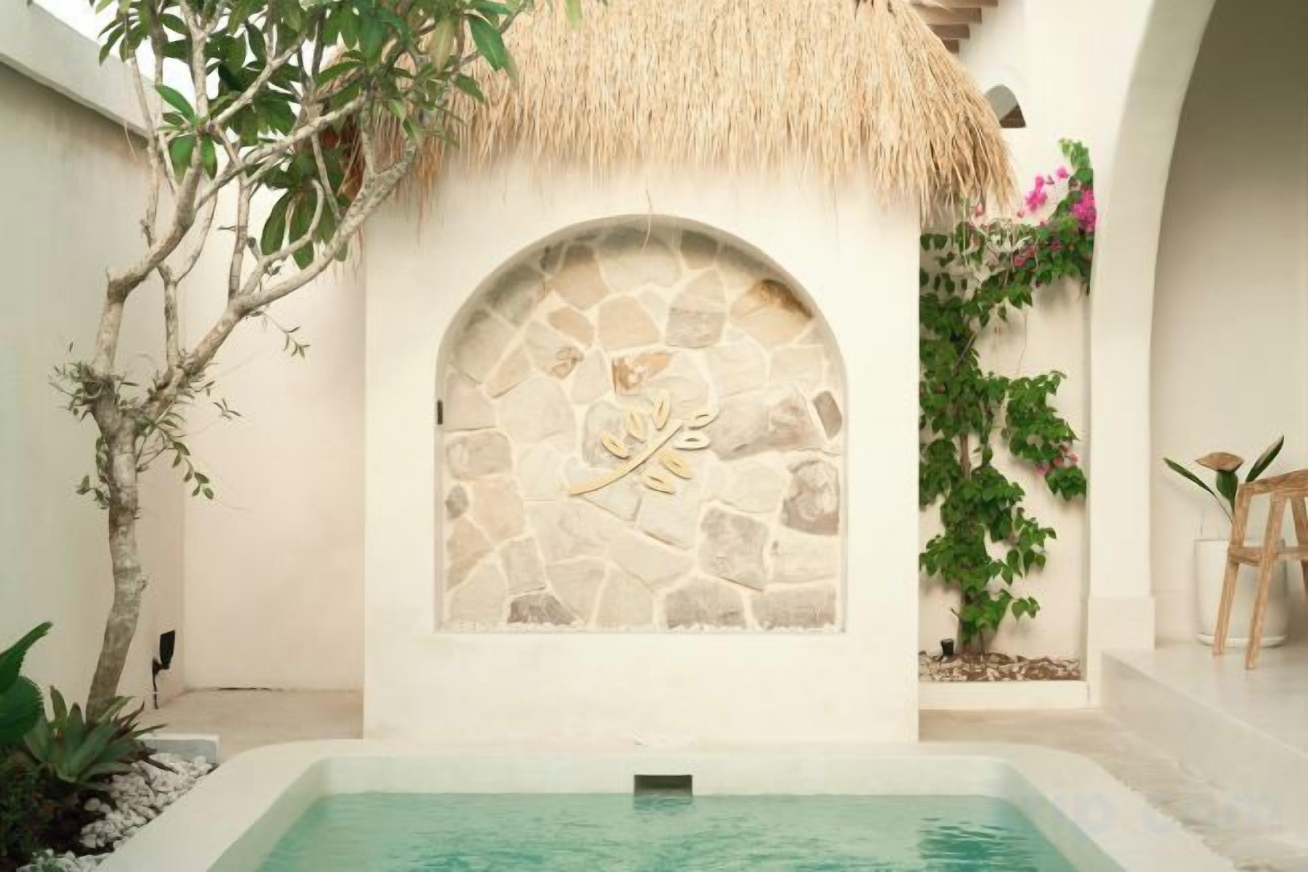 A stone wall with a carved design, a pool, and a thatched roof structure.
