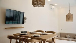 Een moderne eetruimte met een houten tafel gedekt voor zes personen, een wandgemonteerde flatscreen televisie en een hangende pendantlamp.