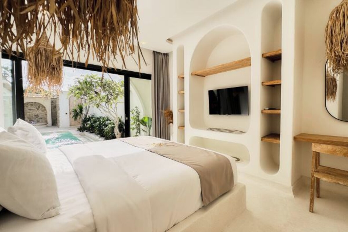 Een moderne slaapkamer met een groot bed, een televisie aan de muur en uitzicht op een zwembad en groen buiten.