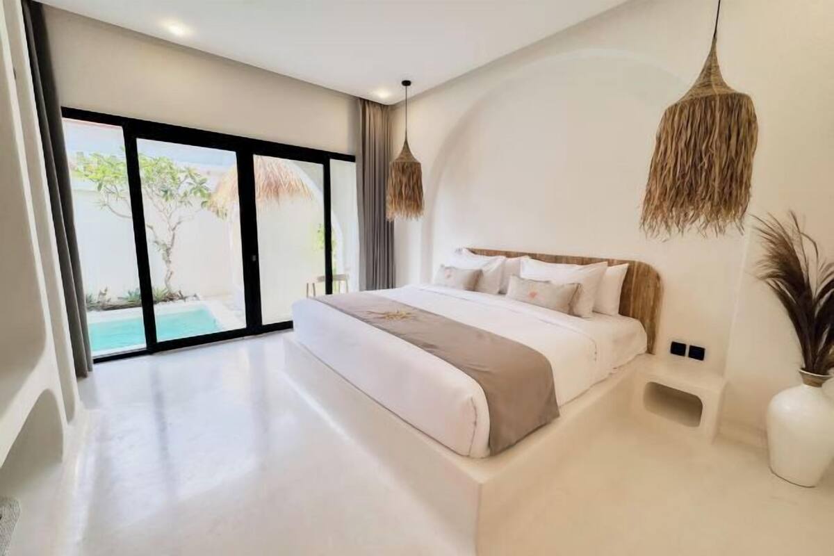 A modern bedroom with a large bed, a view of a swimming pool, and a hanging light fixture.