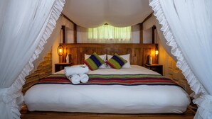 Una cama con sábanas blancas, un edredón colorido a rayas y dos almohadas a rayas. Hay dos mesitas de noche con lámparas.