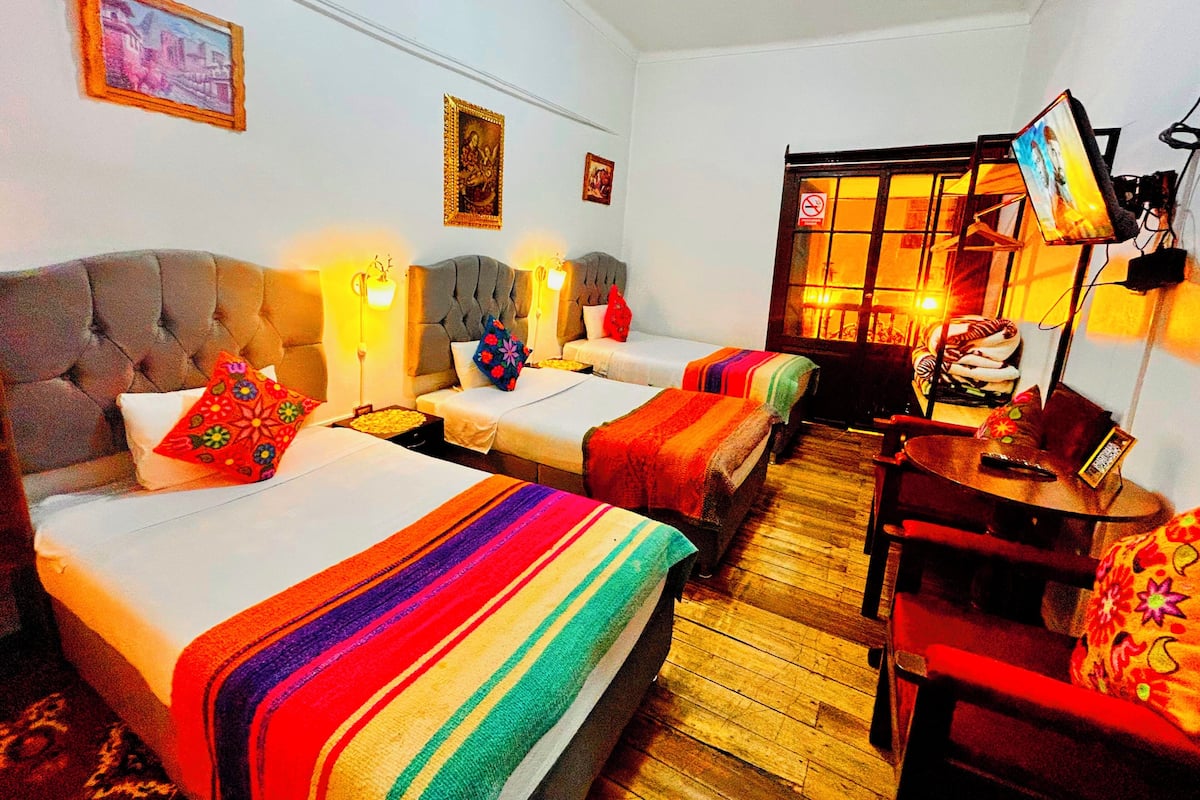 A hotel room with three beds, a wooden floor, a television, and a window with a view.