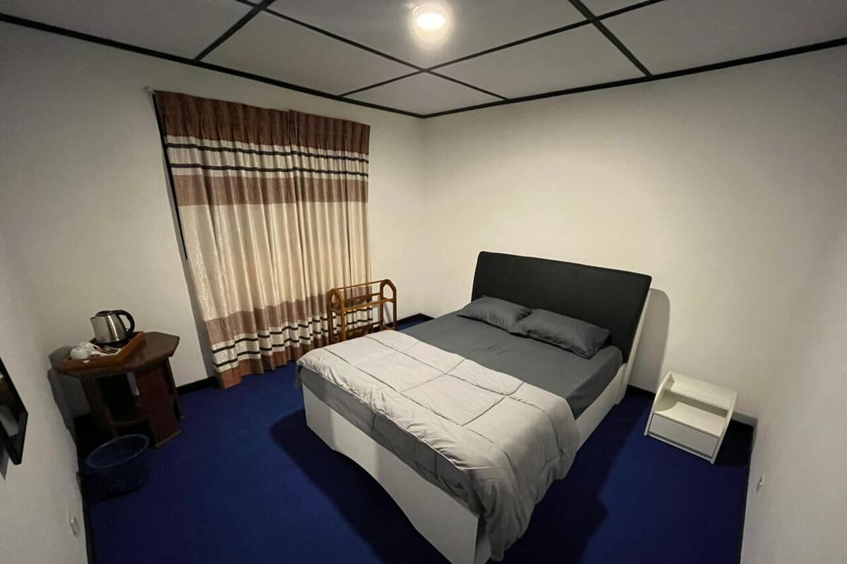 Un dormitorio con cama, mesita de noche, silla y ventana con cortinas.