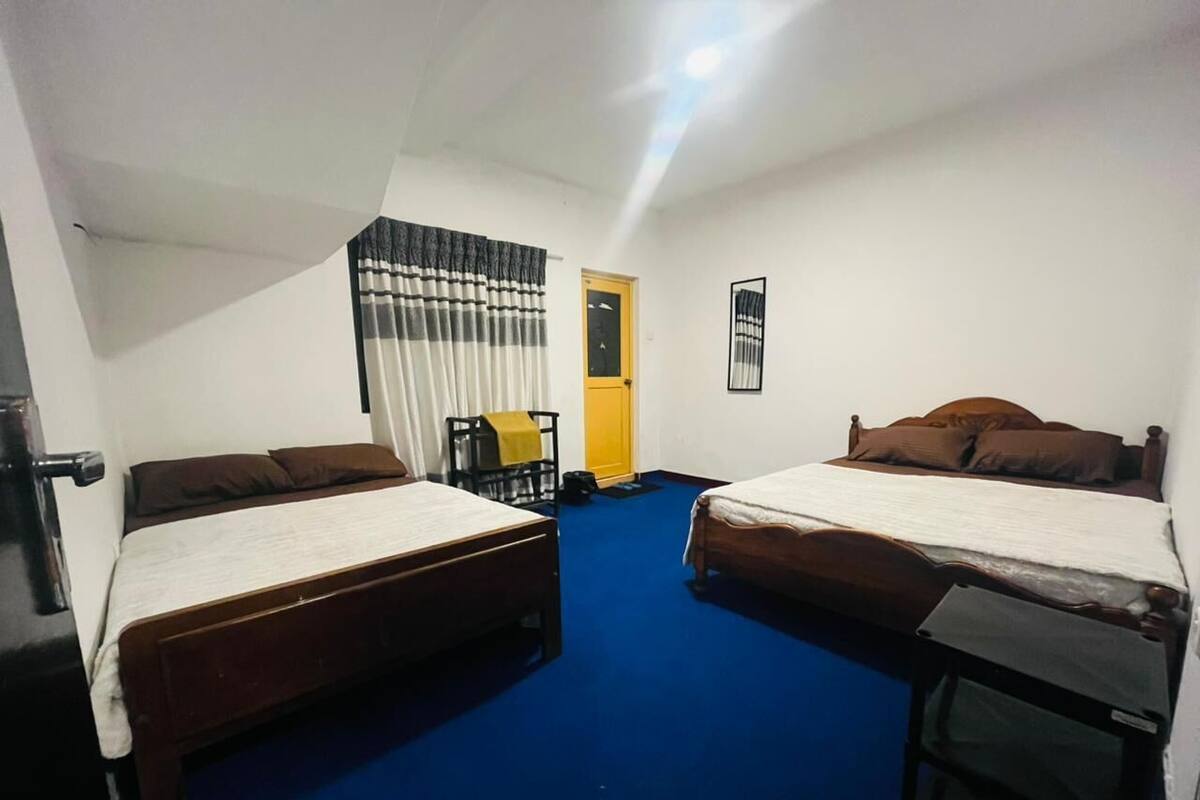 Una habitación con dos camas, una mesita, una silla y una puerta que da a un baño.