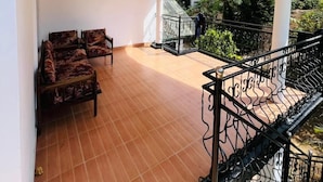 A covered terrace with tiled flooring, a seating area with patterned chairs, and a staircase with black railings. - The Crowns Lodge (Nuwara Eliya)