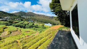 A hillside view of terraced fields, a building with a white exterior, and a clear blue sky. - The Crowns Lodge (Nuwara Eliya)