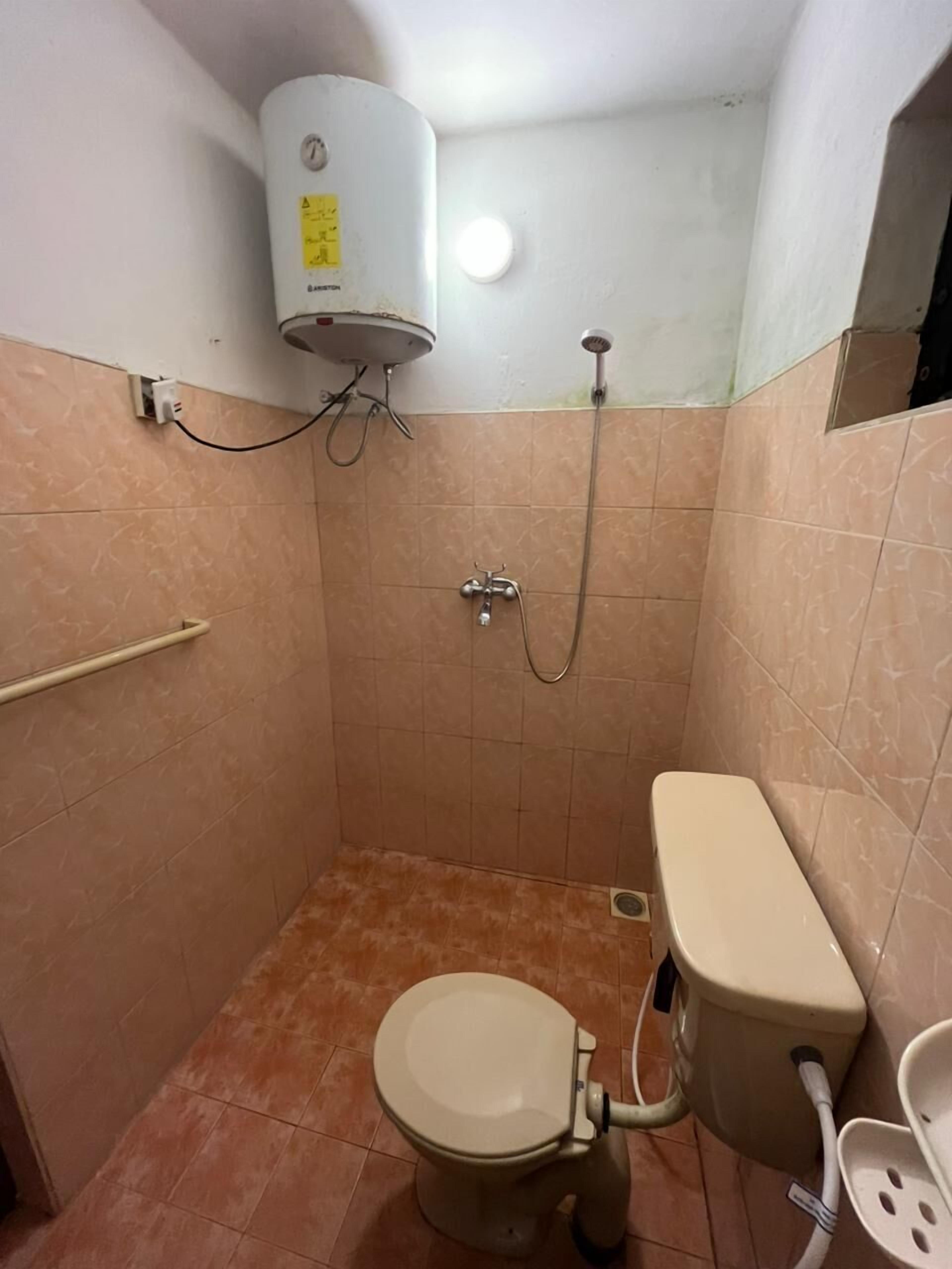 Un baño pequeño con azulejos, que incluye un inodoro, una ducha y un calentador de agua.