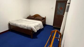 Ein kleines Schlafzimmer mit einem Bett, einem Holzstuhl und einer Tür mit einem Gemälde.