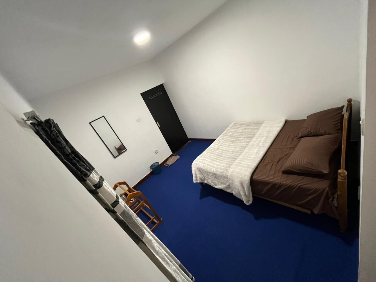 A bedroom with a single bed, a blue carpet, a wooden chair, a small table, and a door.