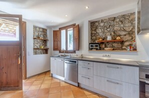 A modern kitchen with stone wall backsplash, wooden cabinets, and a built-in dishwasher. - Stunning Finca with Heated Pool for 8 Guests (Illes Balears)