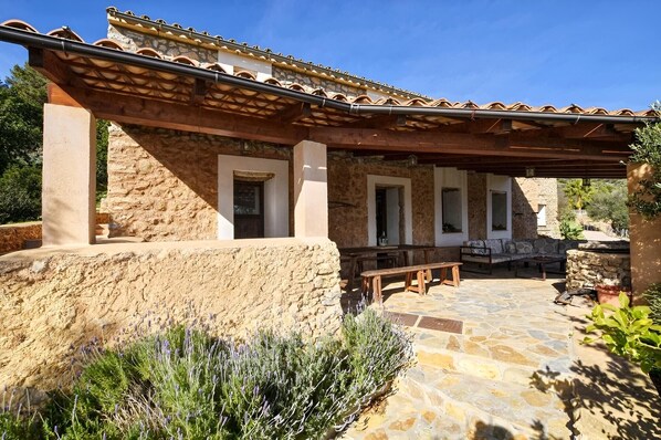 A stone building with a tiled roof, outdoor seating, and a stone patio. - Stunning Finca with Heated Pool for 8 Guests (Illes Balears)