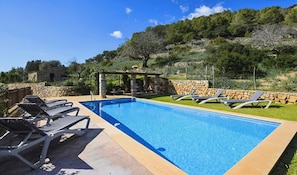 A rectangular swimming pool with clear blue water, surrounded by a stone wall and a grassy area.