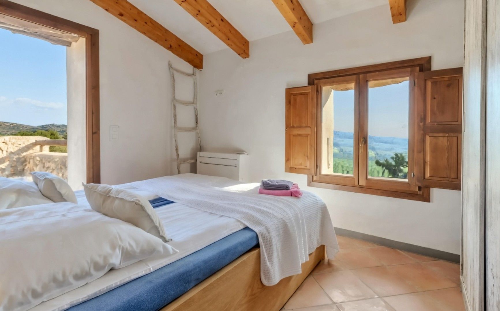 Ein Schlafzimmer mit Bett, Fenster, Holzboden und Blick ins Freie.