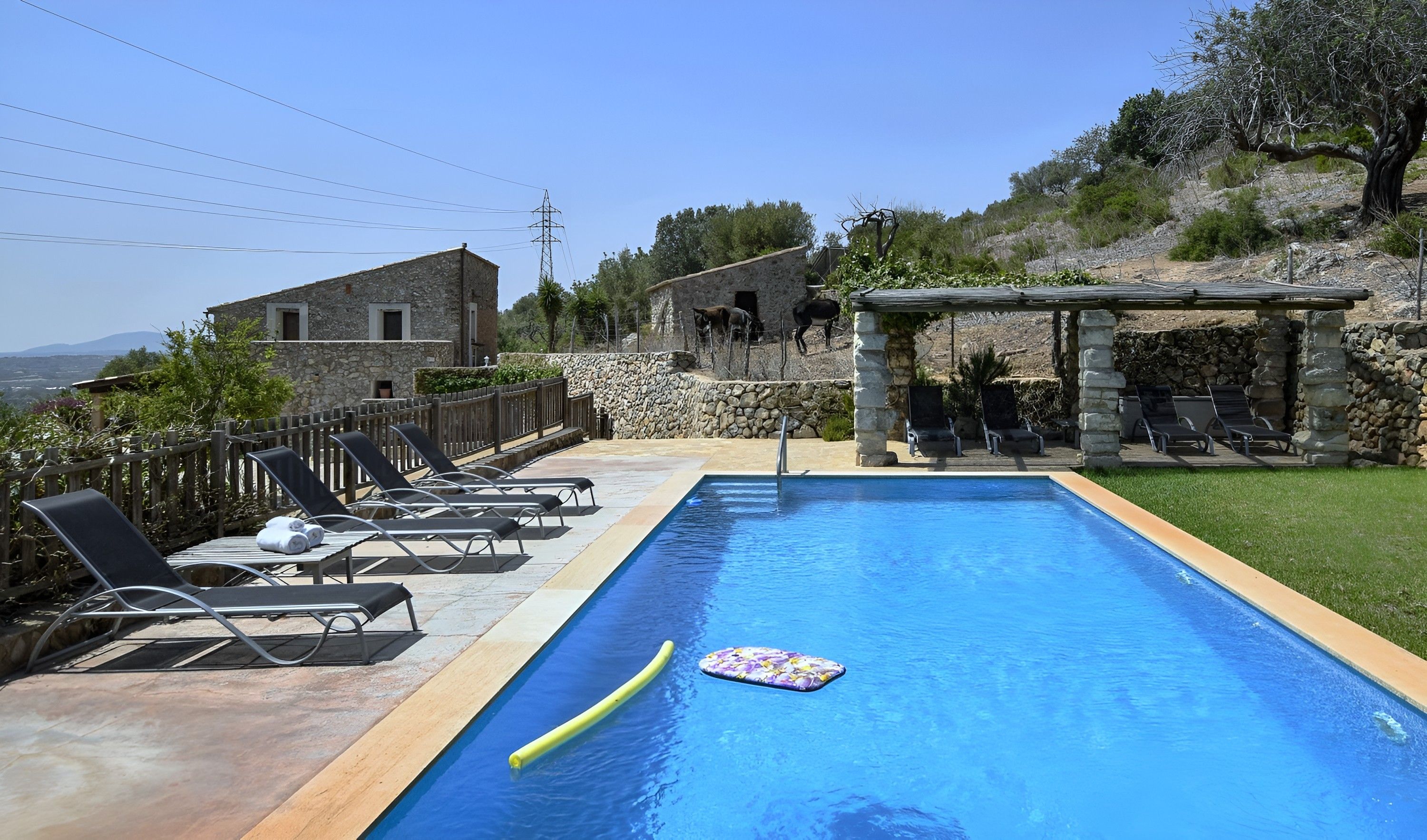 Una piscina con sillas de descanso, un edificio de piedra y vistas al paisaje.