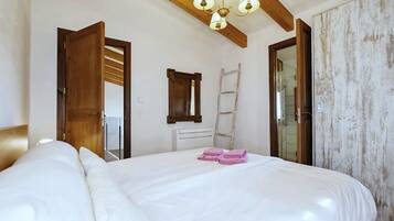 Ett sovrum med en stor säng, synliga träbjälkar, en stege, en spegel och ett vitt element.